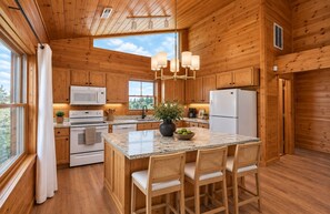 A wooden cabin-style kitchen with granite countertops, a central island with bar stools, a microwave, oven, and refrigerator.