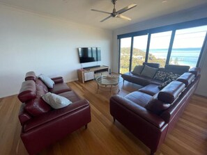 Relax in a serene space with a large flat-screen TV, two comfortable sofas, and a ceiling fan, all set against a stunning ocean view.