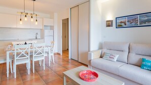 Un soggiorno moderno con un divano, un tavolo da pranzo con sedie, una zona cucina con mobili e una ciotola rossa su un tavolino.