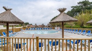 Area piscina con lettini prendisole e ombrelloni di paglia, circondata da una recinzione in legno.