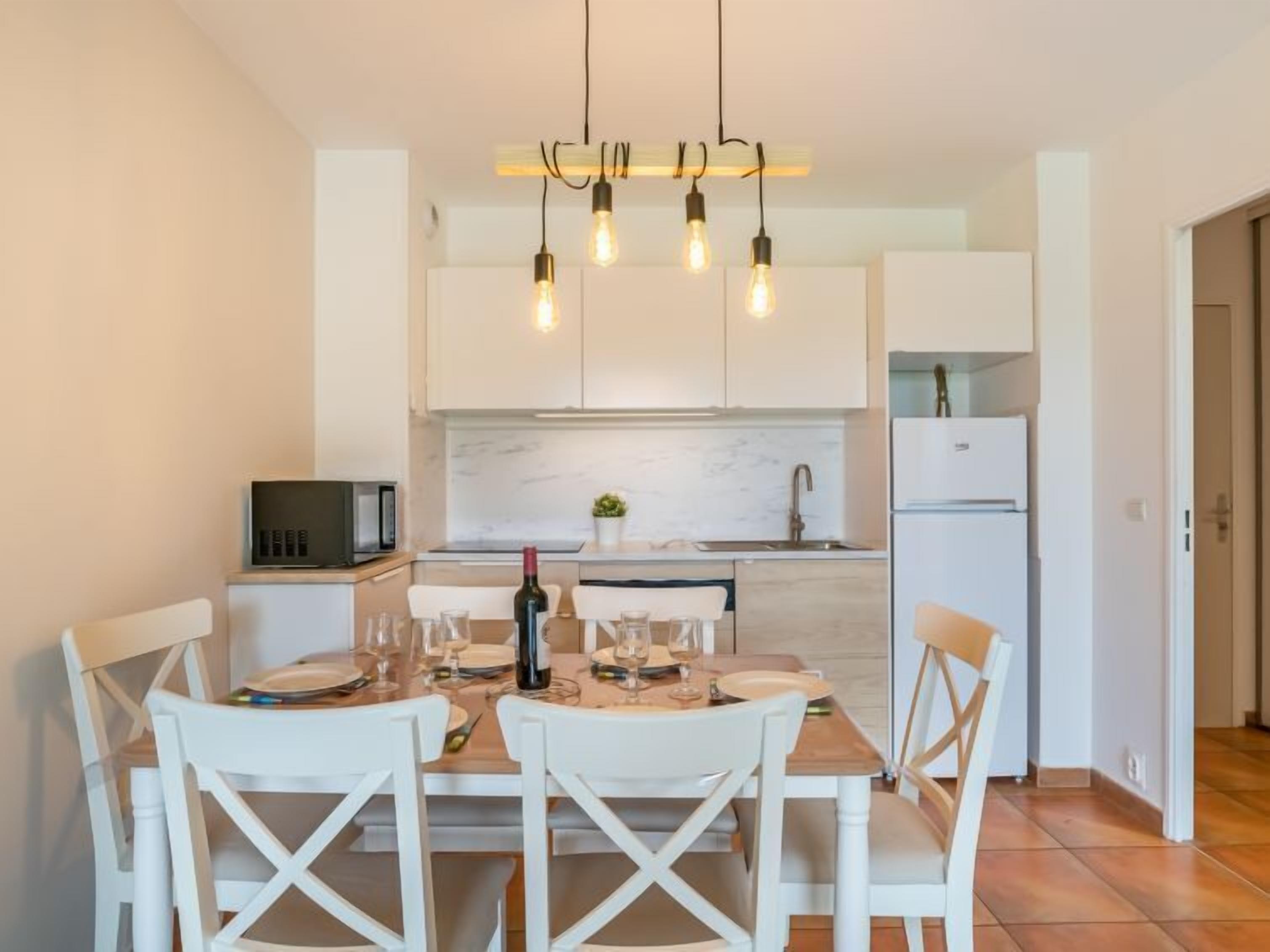 Una cucina moderna con mobili bianchi, una parete protettiva in marmo e un'area pranzo con tavolo in legno e sedie bianche.