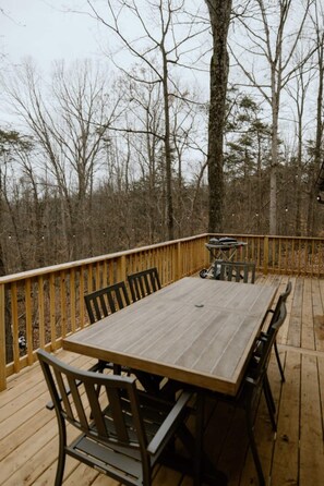 A wooden deck with a table and chairs, surrounded by trees. - The Roost cabin Hocking Hills (with WiFi) (Rockbridge)