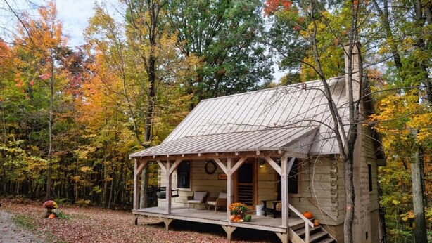 A rustic cabin with a porch, surrounded by autumn foliage.