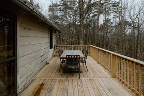 A wooden deck with a table and chairs, surrounded by a wooden railing, overlooking a forested area. - The Roost cabin Hocking Hills (with WiFi) (Rockbridge)