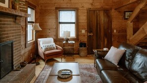 A cozy log cabin interior with a fireplace, leather sofa, and a wooden coffee table. - Tanglewood Cabin in Hocking Hills (with WiFi) (Rockbridge)