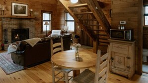 A cozy cabin interior with a fireplace, wooden floors, a dining table with chairs, a sofa, and a staircase. - Tanglewood Cabin in Hocking Hills (with WiFi) (Rockbridge)