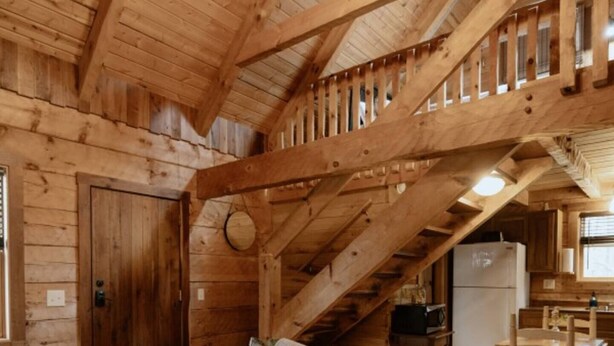 L'intérieur d'un chalet en bois, avec un canapé vert, un pouf capitonné et un escalier menant à un niveau supérieur.