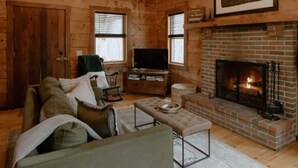 L’intérieur d’une cabane en rondins, avec une cheminée, un canapé, un téléviseur et un lustre.