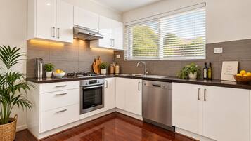 A modern kitchen with white cabinets, a built-in oven, a dishwasher, and a window with blinds.
