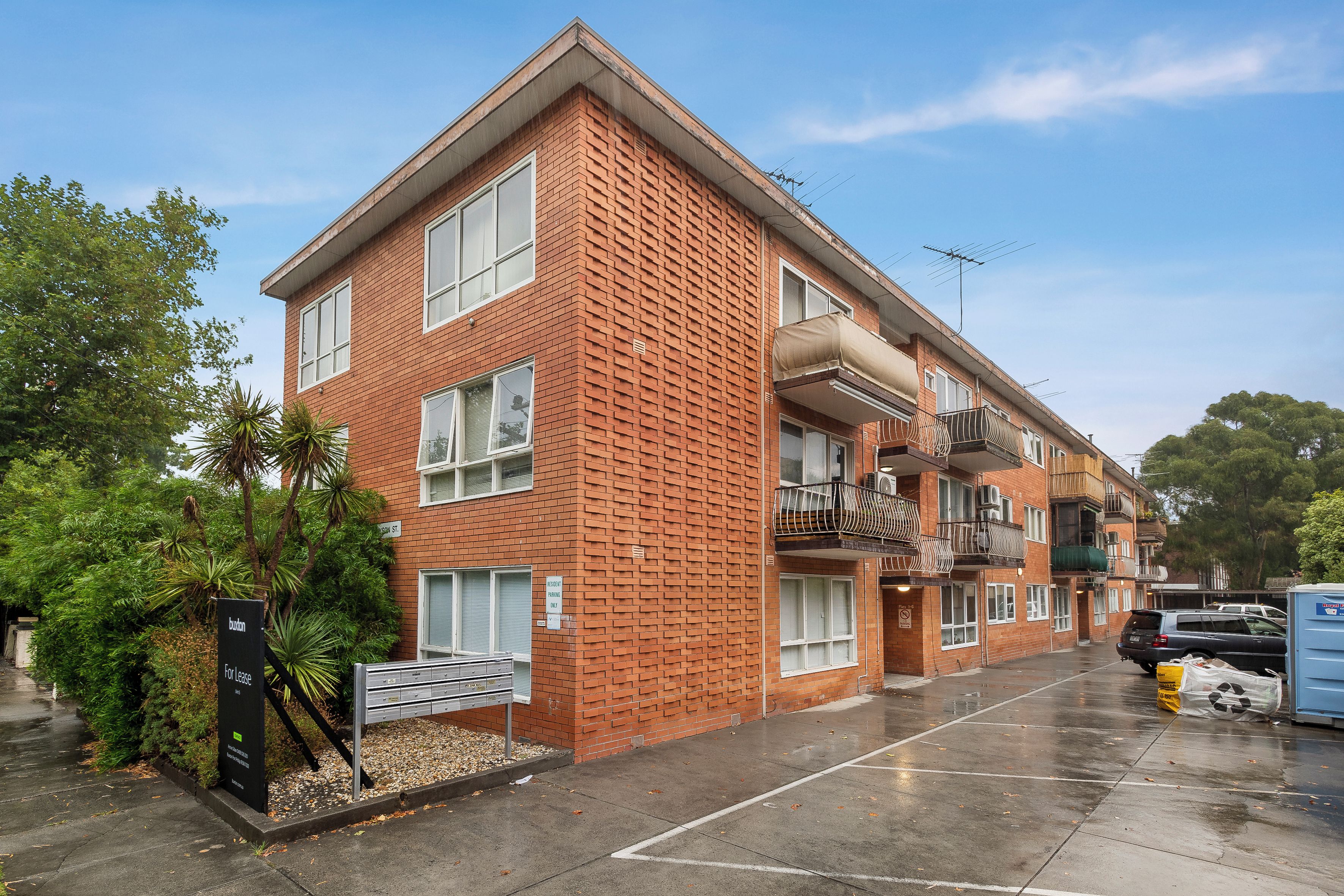 A multi-story residential building with a brick facade, balconies, and a parking area.