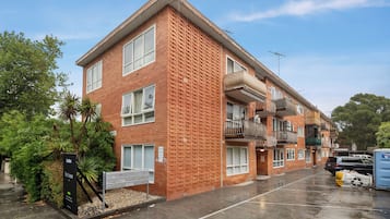 A multi-story residential building with a brick facade, balconies, and a parking area.