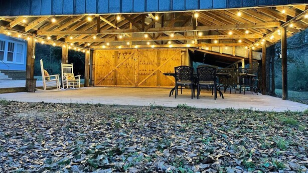 Un porche techado al aire libre con luces colgantes, sillas de madera y un piano.