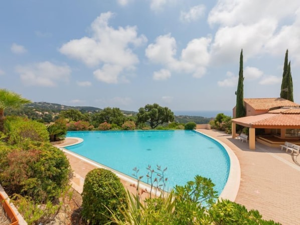 A swimming pool with a curved edge, surrounded by lush greenery and a view of the sea.