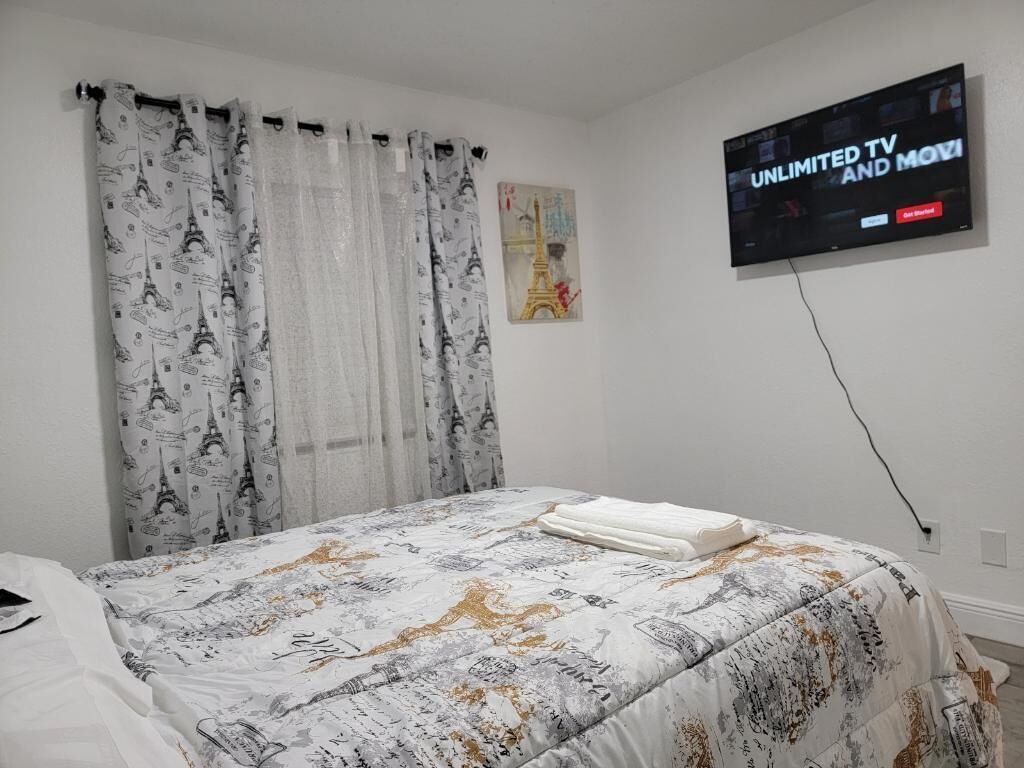 A hotel room with a bed, a TV on the wall, and a painting of the Eiffel Tower.