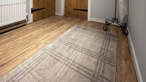 A hallway with two wooden doors, a radiator, and a patterned rug. - “Quirky Cottage” 2 double rooms (Dumfries)