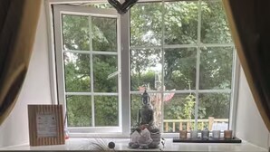 A room with a large window, a statue on the windowsill, and a table with a vase of dried plants. - “Quirky Cottage” 2 double rooms (Dumfries)