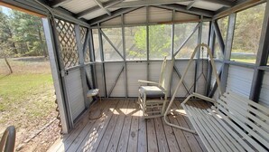 Une véranda couverte avec un plancher en bois, une chaise berçante et un banc.