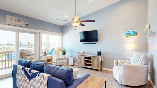 A modern living room with a large window, a ceiling fan, a flat-screen TV, a wooden cabinet, and a cozy armchair.