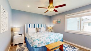 A bedroom with a bed, bedside lamps, a ceiling fan, a window, and artwork on the walls.