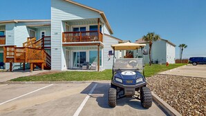 A two-story building with a balcony, a golf cart in the parking lot, and a clear blue sky.