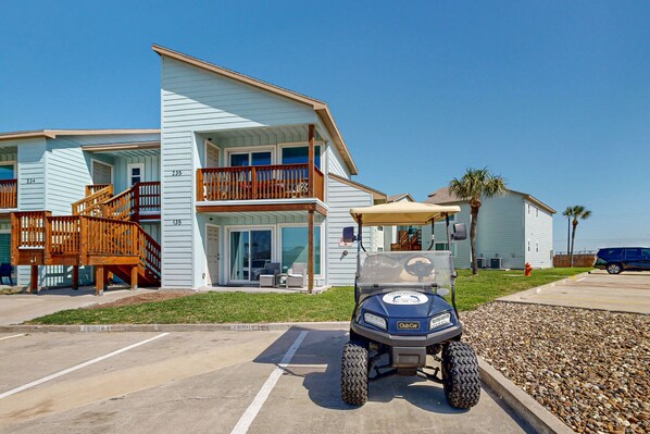 A two-story building with a balcony, a golf cart in the parking lot, and a clear blue sky.