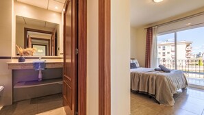 A hotel room with a bathroom, a bed, a balcony with a view of buildings, and a large window. - Golden Beach by Interhome (St Carles de la Ràpita)