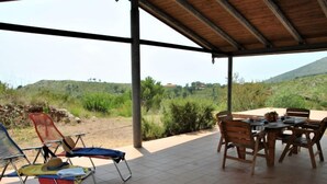 Zona relax all'aperto, riparata, con tavolo e sedie, affacciata su un paesaggio collinare.