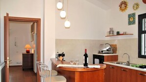Una cucina compatta con isola centrale, sgabelli da bar, una bottiglia di vino e un lavandino.
