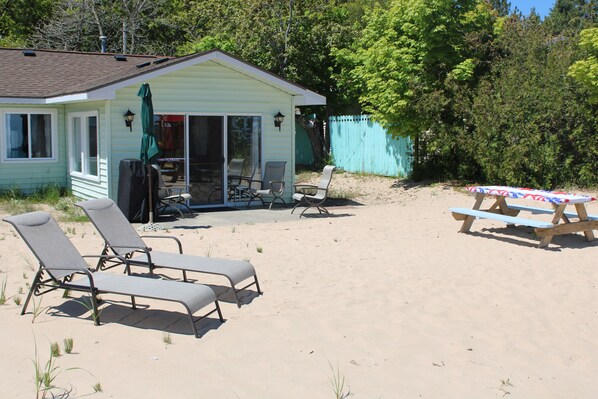 A beach house with a patio, two lounge chairs, a table, and a covered area with a tablecloth.