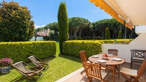 An outdoor patio with a round wooden table and chairs, surrounded by neatly trimmed hedges and a variety of trees. - Green Mar B garden & terrace by Interhome (Pals)