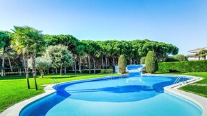A swimming pool with a curved design, surrounded by well-maintained grass and trees. - Green Mar B garden & terrace by Interhome (Pals)