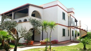 Um edifício branco com varanda, janelas em arco e escadaria que leva ao segundo andar.