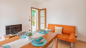 Uma sala de estar moderna com uma mesa de jantar de madeira posta para dois, uma televisão de tela plana e um sofá laranja vibrante.