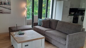 A modern living room with a sofa, a coffee table, and a kitchen area visible through an open door. - Apartment 'Gardensuite Binz' with Pool, Wi-Fi & Terrace (Binz)