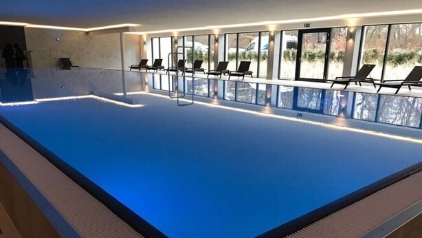 An indoor swimming pool with a clear view of the outside through large windows, a reception area with a counter, and several lounge chairs along the poolside. - Apartment 'Gardensuite Binz' with Pool, Wi-Fi & Terrace (Binz)