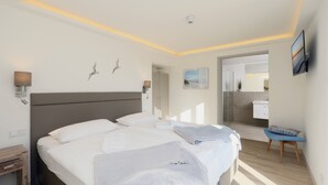 A modern hotel room with a large bed, bedside lamps, a small desk, a chair, and a bathroom visible through an open door. - Apartment 'Gardensuite Binz' with Pool, Wi-Fi & Terrace (Binz)