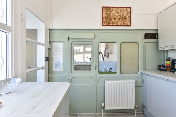Una cucina compatta con un piano di lavoro in marmo, un termosifone bianco e un piccolo finestrino con vista su sedie all'esterno.