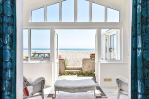 Una stanza con un'ampia finestra vista spiaggia, mobili in vimini e vista mare.