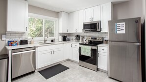 Una cocina moderna con armarios blancos, electrodomésticos de acero inoxidable y un ventanal que proporciona luz natural.