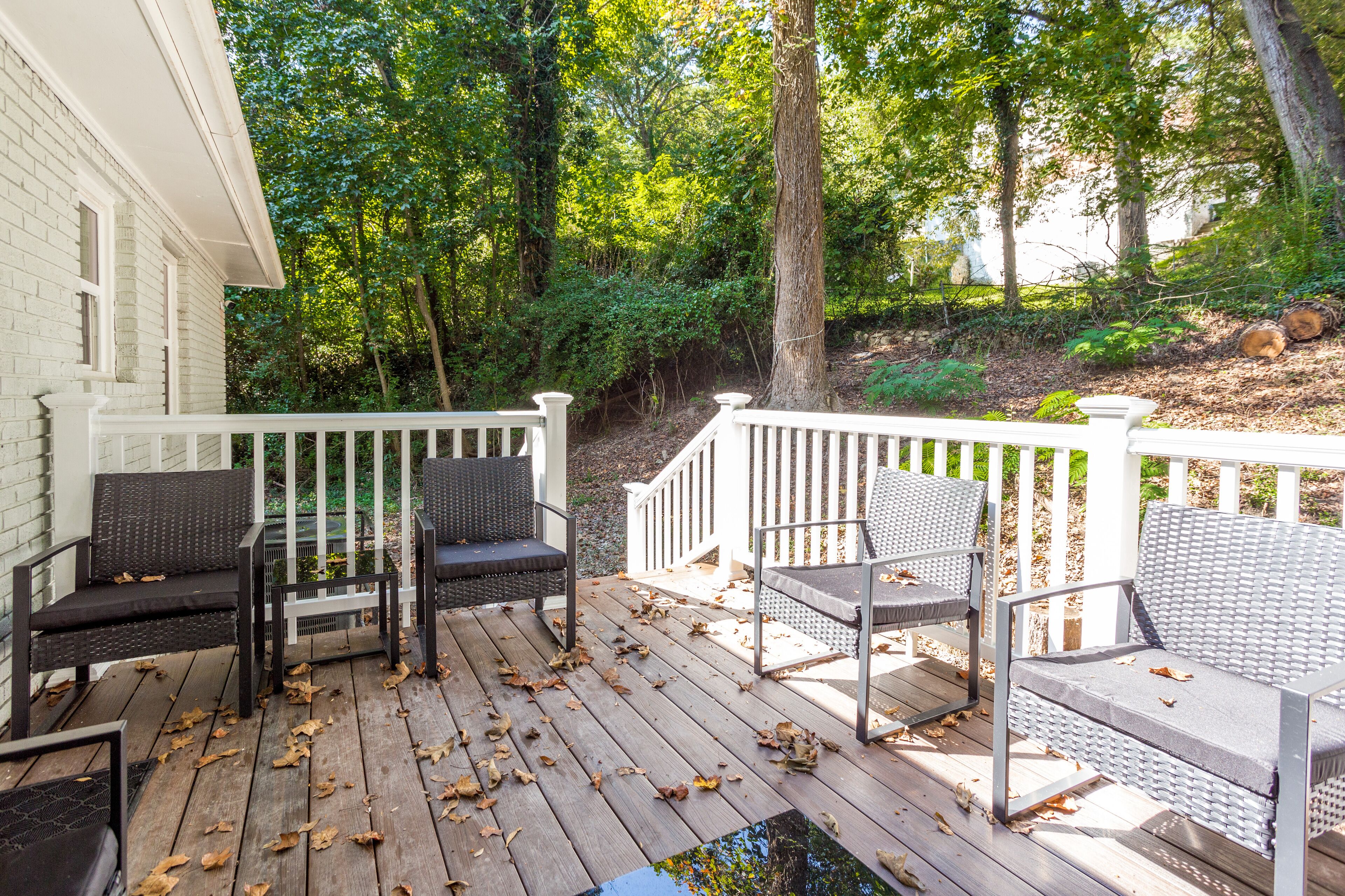 A wooden deck with outdoor furniture, surrounded by a white fence and trees.