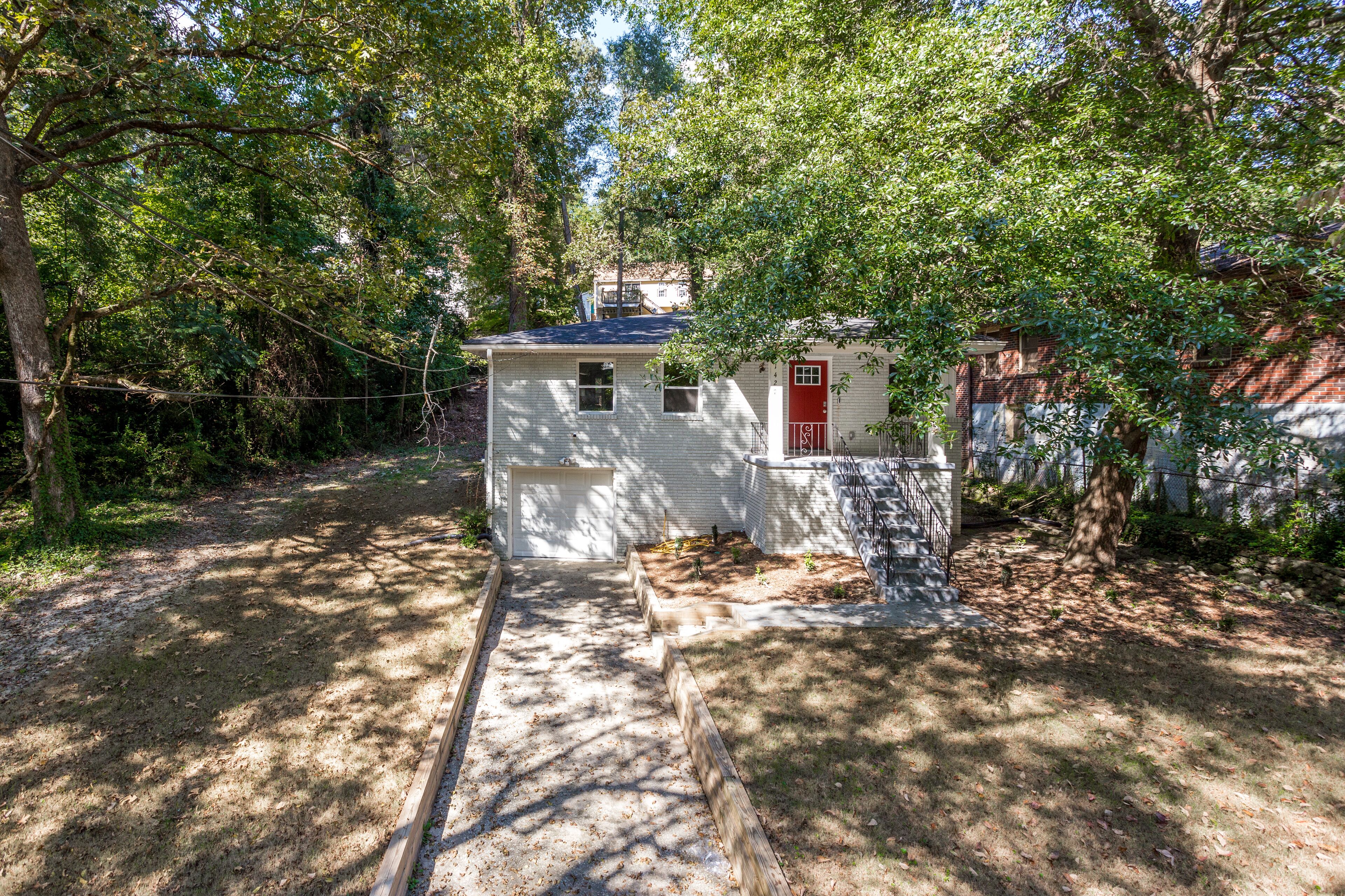 A small house with a red door, surrounded by trees and a wooden fence.