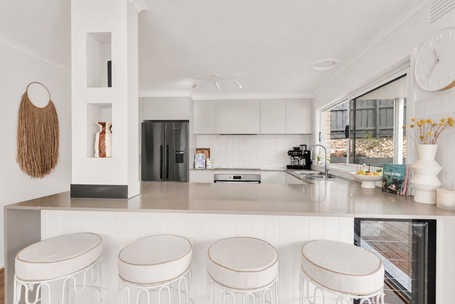 A modern kitchen with a central island, bar stools, a refrigerator, and a coffee machine.