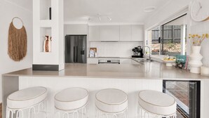 A modern kitchen with a central island, bar stools, a refrigerator, and a coffee machine. - Boutique Retreat Portsea by Ready Set Stay (Portsea)
