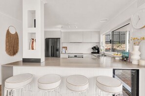 Una cucina moderna con isola centrale, sgabelli da bar, frigorifero e macchina da caffè.
