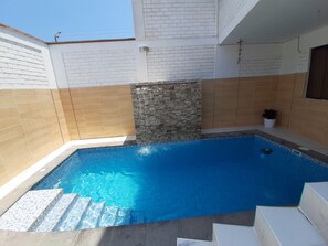 Uma pequena piscina interior com paredes revestidas de azulejos e uma parede decorativa em pedra.