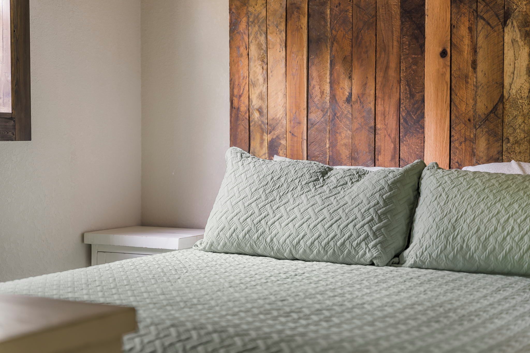 Un dormitorio con cabecera de madera, una mesita de noche blanca y una cama con dos almohadas.