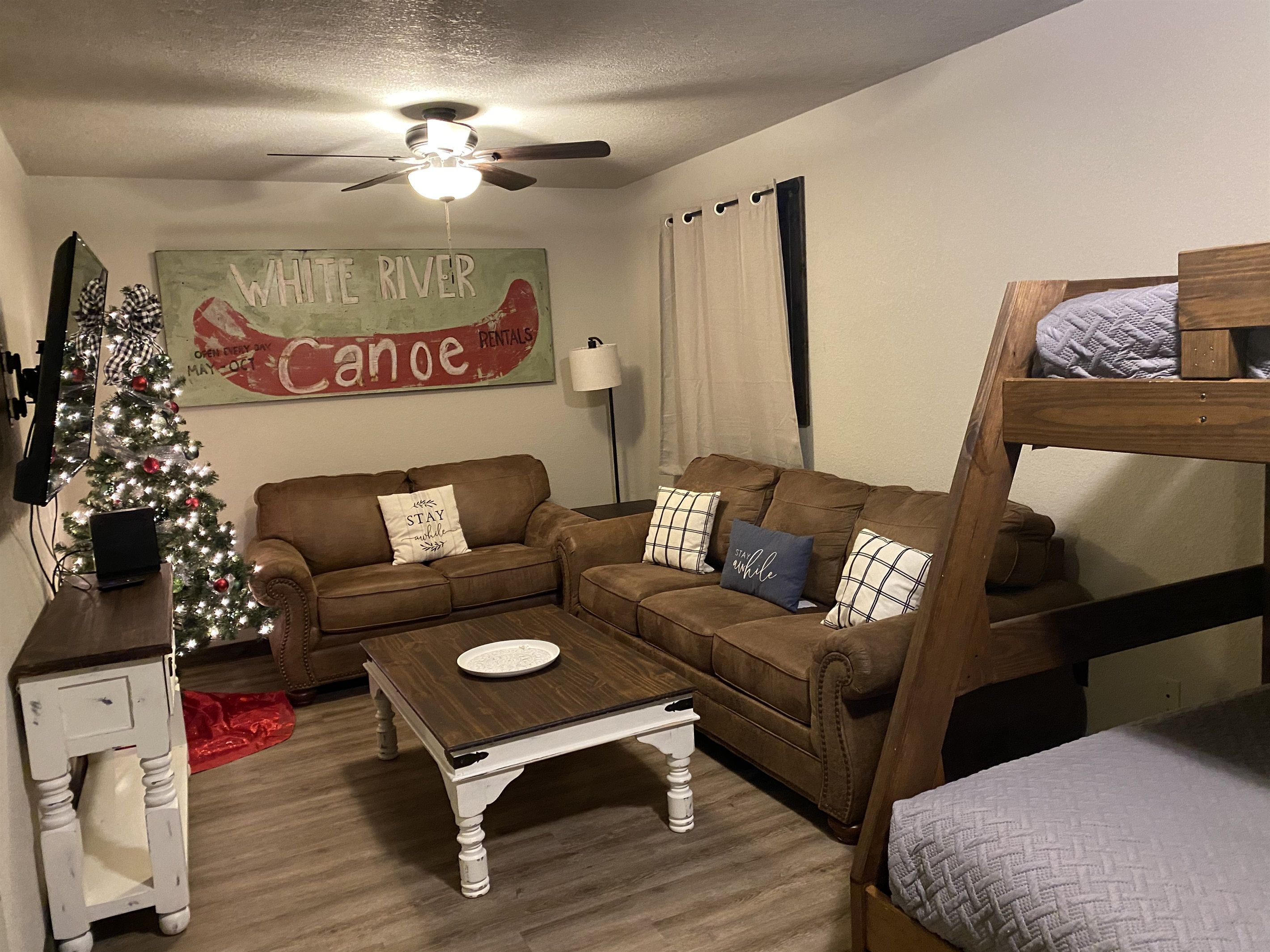 Una sala acogedora con un sofá marrón, una mesa de centro de madera, un árbol de Navidad y una cama litera.