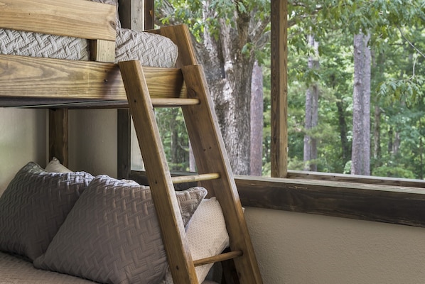 Een stapelbed met een houten trap, twee kussens en een raam met uitzicht op een bos.