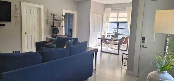 Relax in this stylish living room with a sofa, dining area, and mounted TV.