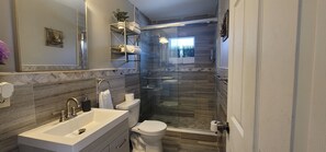 Features a sleek sink, toilet, and glass-enclosed shower area with a patterned tile design and decorative mirror.